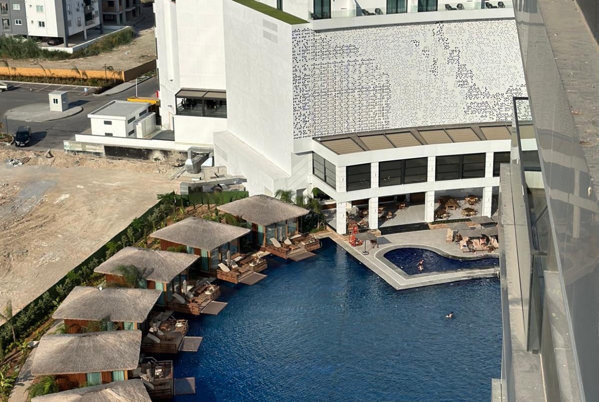 kıbrıs Yüksek beyaz binaların yanında sazdan kabanalar ve şezlonglar bulunan modern bir otelin havuz alanının havadan görünümü. Ötesinde okyanus görülüyor. İskele Long Beach satılık daire arayanlar veya Kuzey Kıbrıs gayrimenkulde Aysan Giti emlak'ı keşfetmek için mükemmeldir. aysan_giti