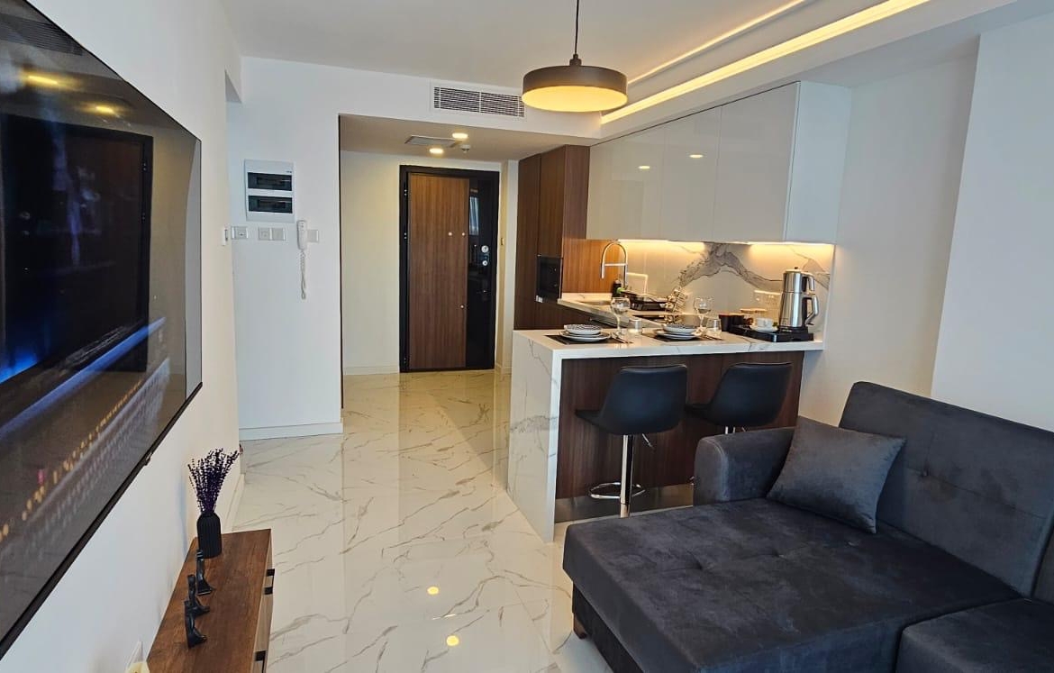 kıbrıs Gri kanepe, duvara monte TV, mermer zemin ve şık mutfak tezgahı ile modern açık konsept daire. İskele Long Beach satılık daire seçeneklerini geniş aydınlatma ve kullanışlı bir yemek düzenine sahip aydınlık bir alanda arayanlar için idealdir. aysan_giti