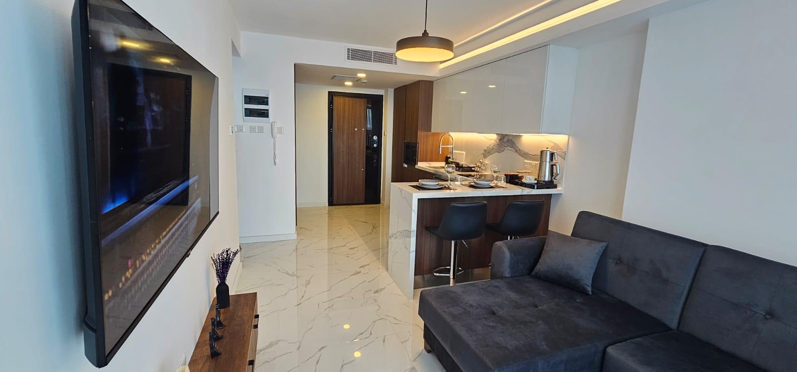 kıbrıs Gri kanepe, duvara monte TV, mermer zemin ve şık mutfak tezgahı ile modern açık konsept daire. İskele Long Beach satılık daire seçeneklerini geniş aydınlatma ve kullanışlı bir yemek düzenine sahip aydınlık bir alanda arayanlar için idealdir. aysan_giti