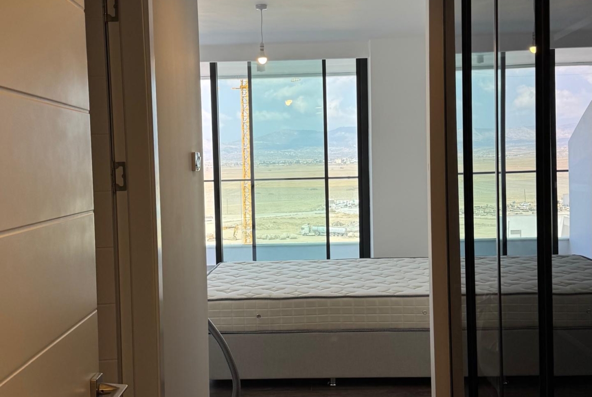 kıbrıs Koyu ahşap zeminli bir koridor, Kuzey Kıbrıs satılık daire arayanlar için mükemmel olan okyanus manzaralı büyük pencerelere sahip aydınlık bir yatak odasına açılmaktadır. Sağ tarafta yataksız bir yatak ve aynalı dolap kapakları var. Dışarıdan ışık giriyor. aysan_giti