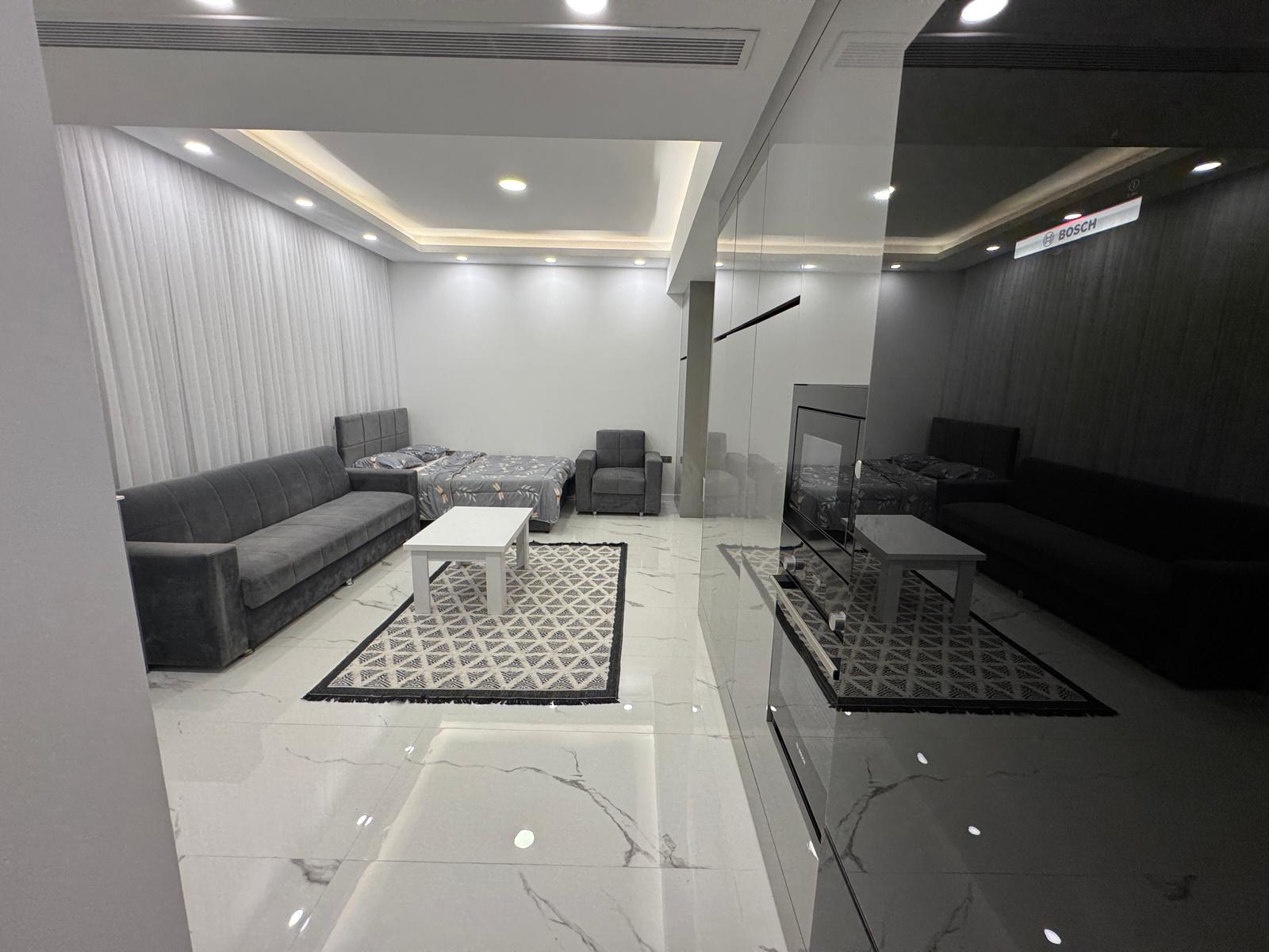 kıbrıs Gri kanepeler, beyaz bir sehpa, desenli halılar ve beyaz fayans döşemeli modern bir oturma odası. Odanın tavan ışıkları ve duvarları gömme olup bir tarafında mobilyaları yansıtan cam bir bölme bulunmaktadır. aysan_giti kıbrıs Gri kanepeler, beyaz bir sehpa, desenli halılar ve beyaz fayans döşemeli modern bir oturma odası. Odanın tavan ışıkları ve duvarları gömme olup bir tarafında mobilyaları yansıtan cam bir bölme bulunmaktadır. aysan_giti