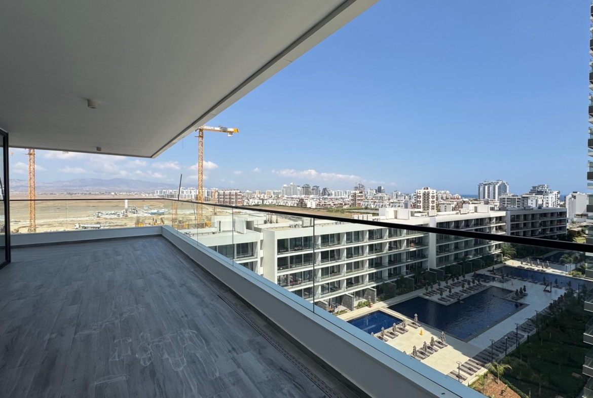 kıbrıs Modern apartmanlara, sonsuzluk havuzuna ve Grand Sapphire Resort & Residence kumarhanesine, inşaat vinçlerine ve masmavi bir gökyüzü altında uzaktaki şehir manzarasına bakan cam korkuluklu geniş bir balkondan görünüm. aysan_giti