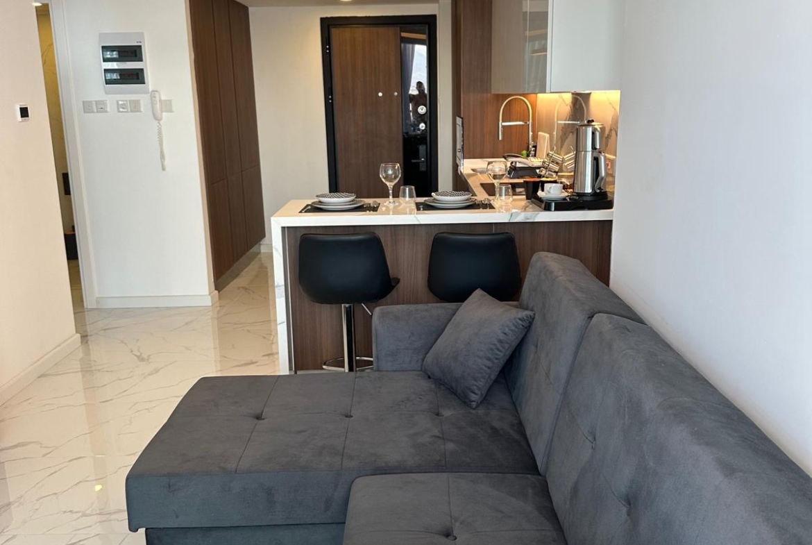 kıbrıs Koyu gri kesitli kanepe, ahşap yan sehpa ve bir ada ile iki siyah bar taburesi içeren mutfak alanına sahip modern stüdyo daire; mermer zeminli minimalist dekor - İskele Long Beach kiralık daire arayanlar için mükemmel. aysan_giti
