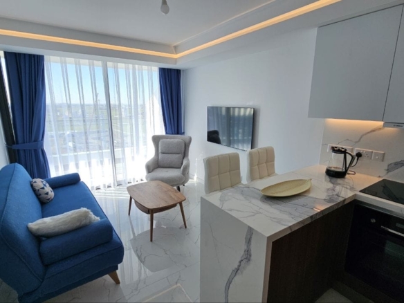 kıbrıs Mavi bir kanepe, koltuk, küçük ahşap masa, mermer tarzı tezgahlar, beyaz bar tabureleri, duvara monte TV ve doğal ışık alan mavi perdeli büyük pencereler içeren modern oturma odası ve mutfak. aysan_giti