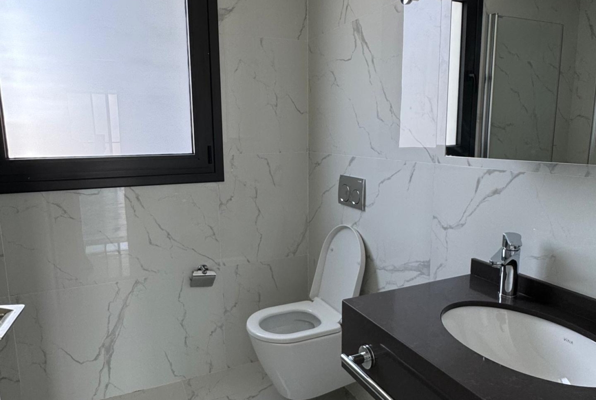 kıbrıs Grand Sapphire Resort & Residence Kıbrıs'ta 7 yıldızlı otel konseptinde yaşam Kıbrıs için tasarlanmış beyaz mermer duvarlar ve zemin, duvara monte tuvalet ve koyu renkli tezgah üstü lavabonun üzerinde büyük bir aynadan oluşan modern banyo. aysan_giti