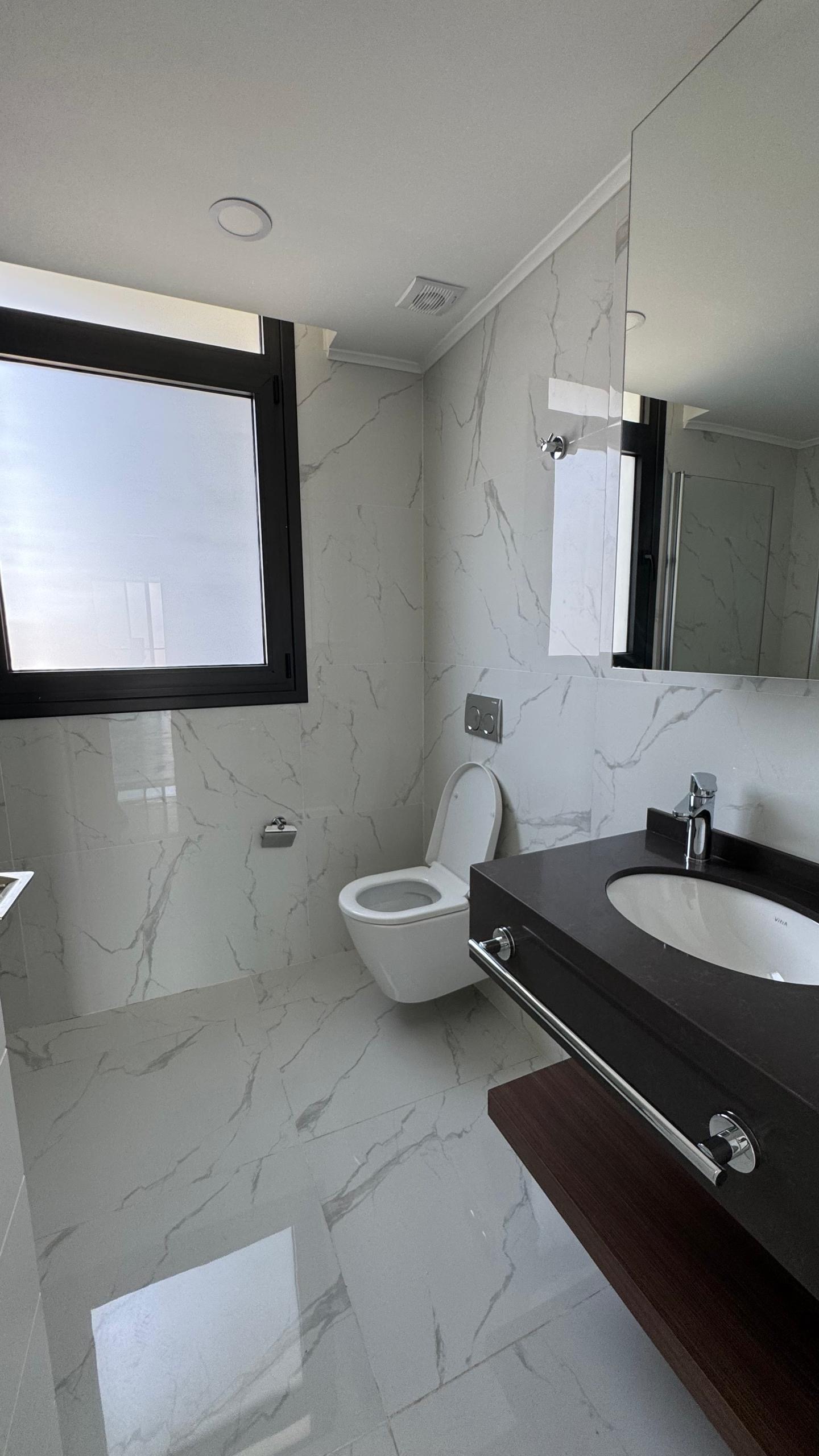 kıbrıs Grand Sapphire Resort & Residence Kıbrıs'ta 7 yıldızlı otel konseptinde yaşam Kıbrıs için tasarlanmış beyaz mermer duvarlar ve zemin, duvara monte tuvalet ve koyu renkli tezgah üstü lavabonun üzerinde büyük bir aynadan oluşan modern banyo. aysan_giti