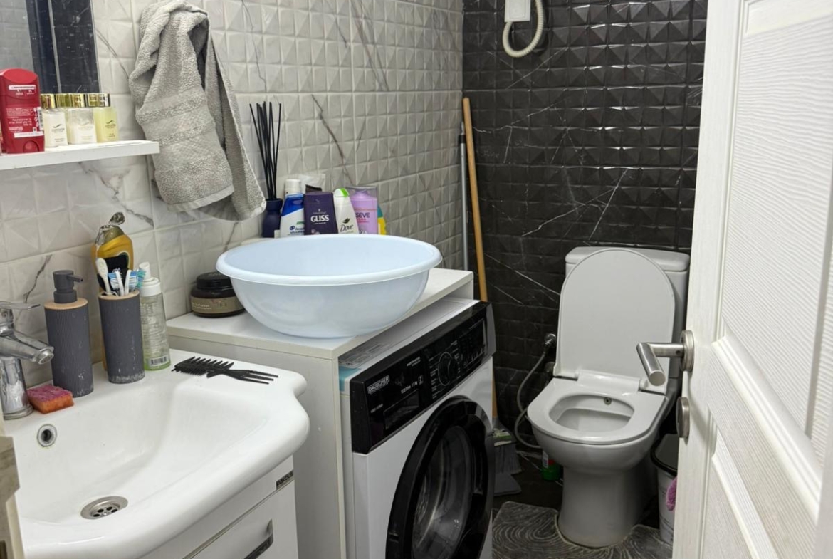 kıbrıs Lavabo, çamaşır makinesi, tuvalet ve su ısıtıcısının bulunduğu küçük bir banyo. Tuvalet malzemeleri ve temizlik malzemeleri raflarda, büyük bir lavabo ise çamaşır makinesinin üzerinde yer alıyor. Duvarlarda gri tonlarda dokulu karolar var. aysan_giti