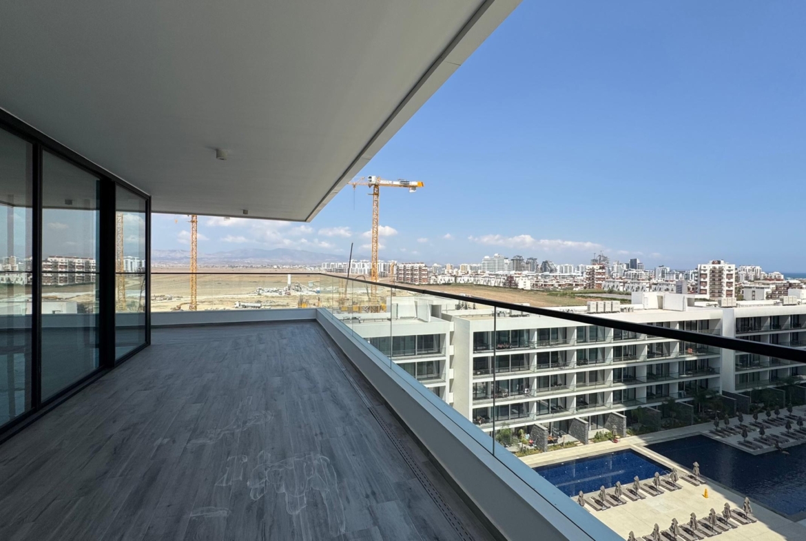 kıbrıs Cam korkuluklara sahip geniş ve modern bir balkon, masmavi bir gökyüzü altında 7 yıldızlı otel konseptinde yaşam Kıbrıs sunan birden fazla apartmanla çevrili Grand Sapphire Resort & Residence Kıbrıs'ın havuzuna ve şezlonglarına bakmaktadır. aysan_giti
