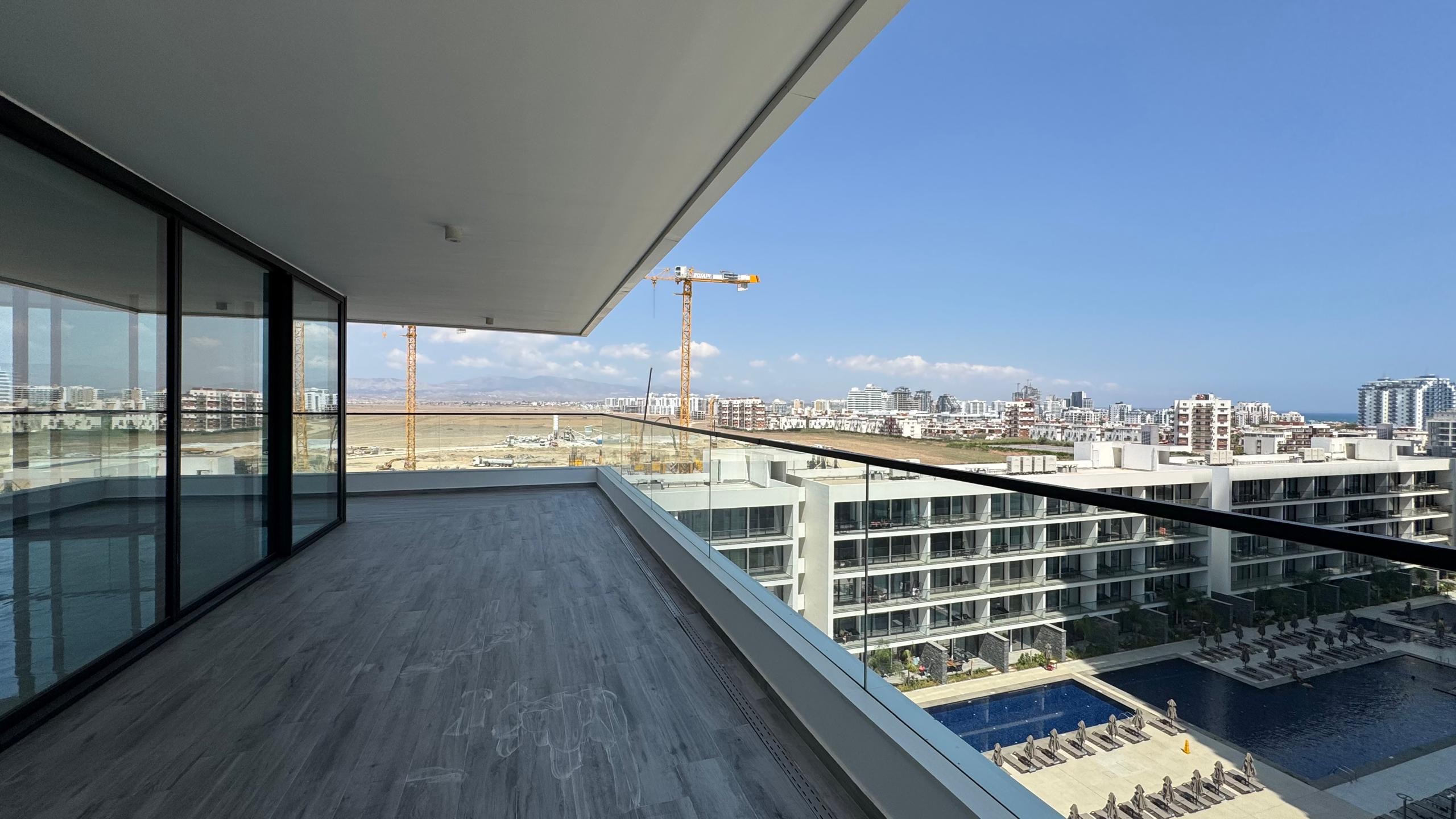 kıbrıs Cam korkuluklara sahip geniş ve modern bir balkon, masmavi bir gökyüzü altında 7 yıldızlı otel konseptinde yaşam Kıbrıs sunan birden fazla apartmanla çevrili Grand Sapphire Resort & Residence Kıbrıs'ın havuzuna ve şezlonglarına bakmaktadır. aysan_giti