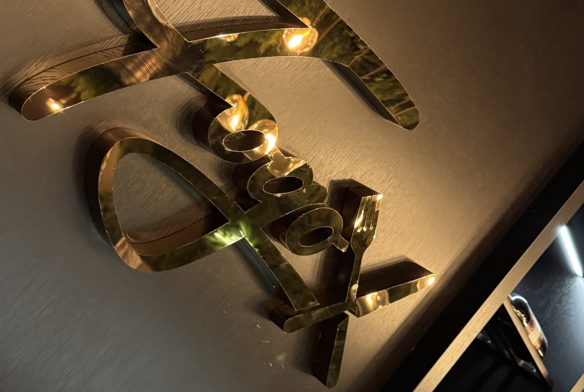 kıbrıs Karanlık bir duvara monte edilmiş altın metalik harfler, yumuşak bir aydınlatma ile aydınlatılmış. Aşağıda, raflarda modern ve lüks bir ortamda şişeler sergileniyor - İskele Long Beach satılık daire veya Kuzey Kıbrıs gayrimenkul yatırımlarıyla ilgilenenler için mükemmel. aysan_giti