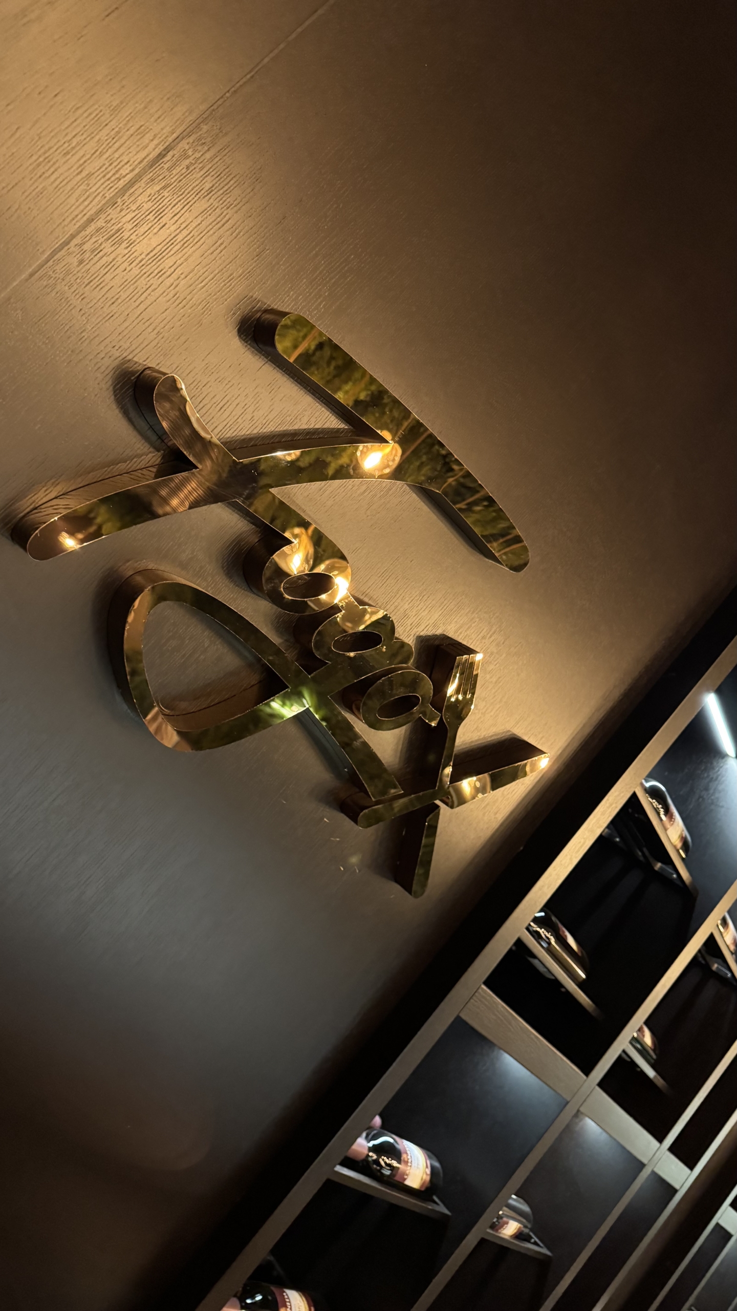 kıbrıs Karanlık bir duvara monte edilmiş altın metalik harfler, yumuşak bir aydınlatma ile aydınlatılmış. Aşağıda, raflarda modern ve lüks bir ortamda şişeler sergileniyor - İskele Long Beach satılık daire veya Kuzey Kıbrıs gayrimenkul yatırımlarıyla ilgilenenler için mükemmel. aysan_giti