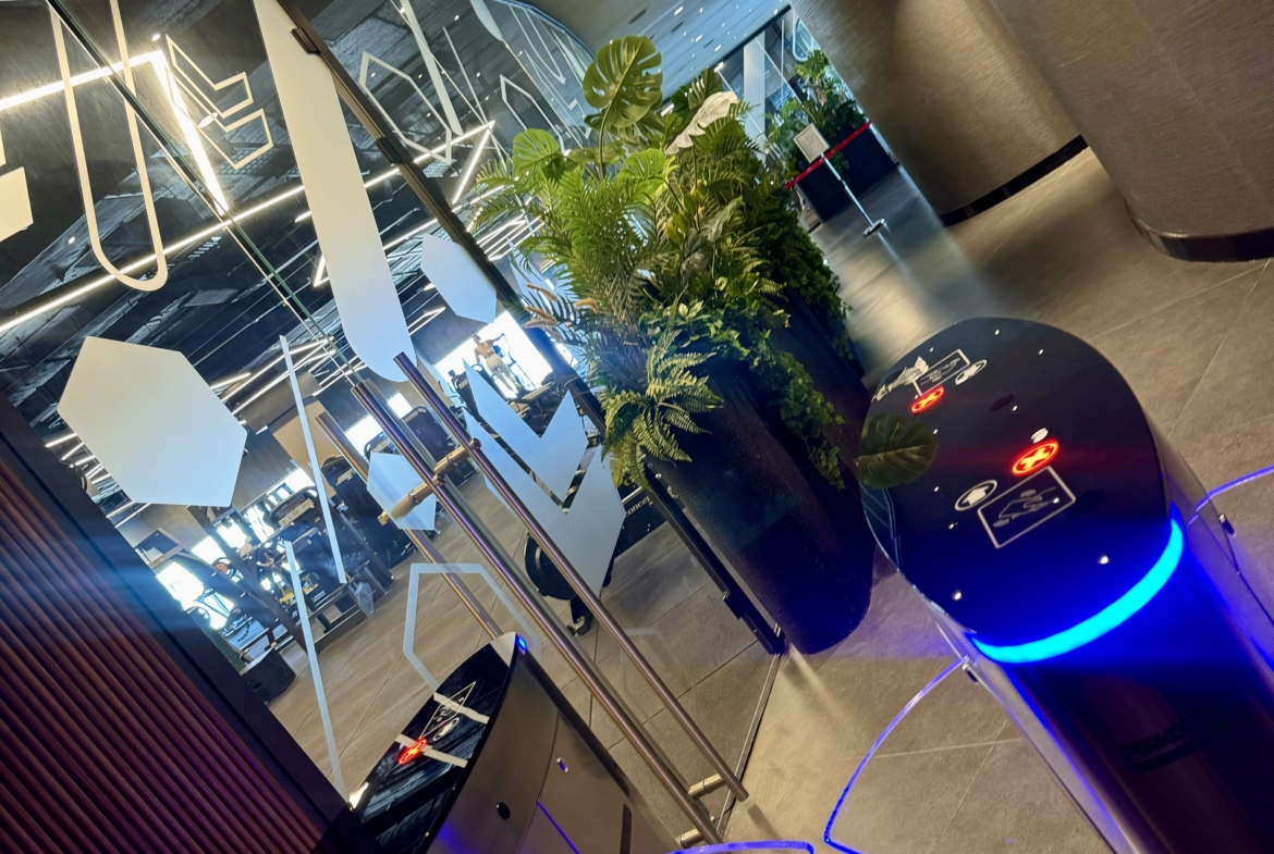 kıbrıs Cam kapılı modern bir ofis girişi, mavi renkte parlayan turnikeler ve ortada büyük bir saksı ile sizi karşılıyor. Şık, kavisli duvarlar ve çağdaş dekor, lüks Kuzey Kıbrıs gayrimenkul alanlarının tarzını çağrıştırıyor. aysan_giti