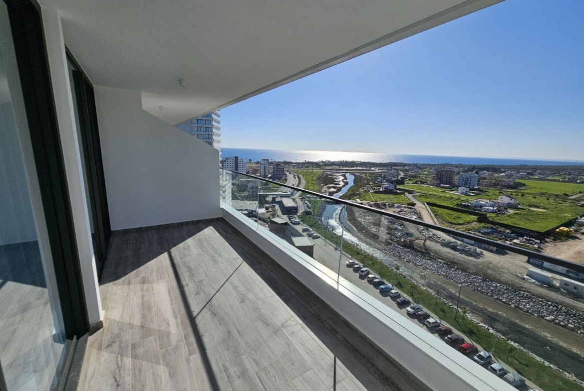kıbrıs Cam korkuluklu modern apartman balkonu, masmavi bir gökyüzünün altında kıyı şehir manzarasına, yeşil alanlara, binalara ve denize bakıyor. Güneş ışığı karo zemin üzerinde gölgeler oluşturuyor. aysan_giti