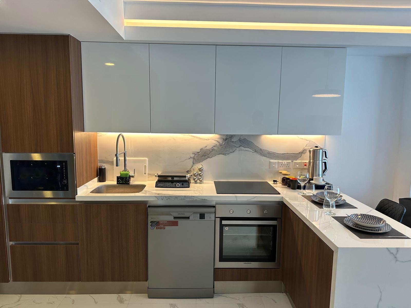 kıbrıs Ahşap ve beyaz dolaplar, mermer backsplash, ankastre fırın, set üstü ocak, bulaşık makinesi, mikrodalga fırın ve dolap altı aydınlatmalı şık tezgahlara sahip modern mutfak, şık bir Kuzey Kıbrıs satılık daire için mükemmeldir. aysan_giti