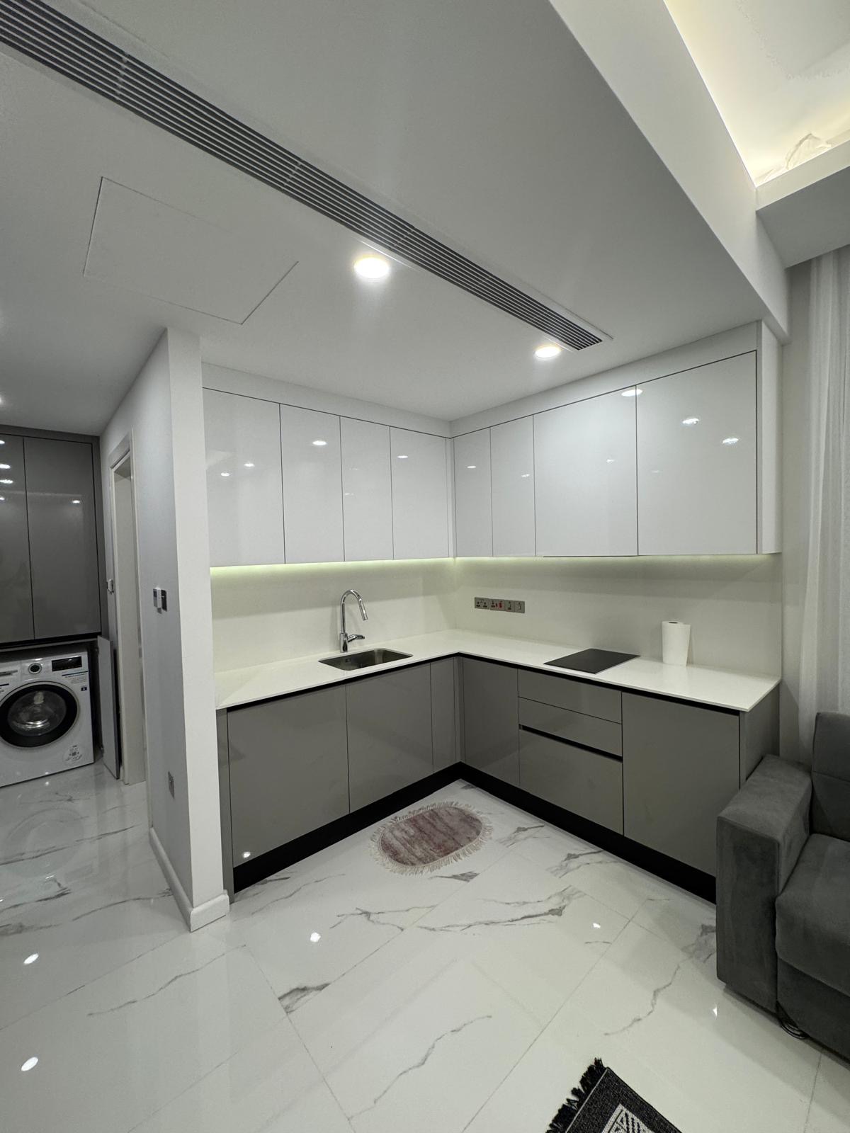 kıbrıs Parlak beyaz ve gri dolaplar, ankastre ocak, lavabo, dolap altı aydınlatması ve mermer zeminiyle modern, minimalist bir mutfak. Bitişik odada bir çamaşır makinesi görülebilir. aysan_giti kıbrıs Parlak beyaz ve gri dolaplar, ankastre ocak, lavabo, dolap altı aydınlatması ve mermer zeminiyle modern, minimalist bir mutfak. Bitişik odada bir çamaşır makinesi görülebilir. aysan_giti