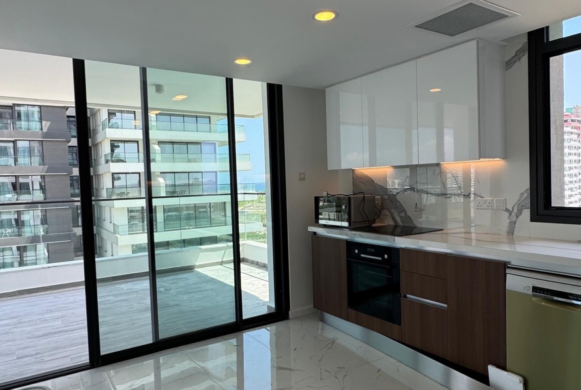 kıbrıs Parlak mermer zeminler, beyaz ve ahşap dolaplar, ankastre cihazlar ve manzaralı bir balkona açılan büyük cam kapılar içeren modern mutfak, İskele Long Beach yakınında şık bir Kuzey Kıbrıs kiralık daire arayanlar için mükemmeldir. aysan_giti