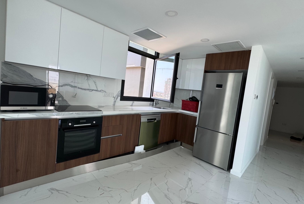 kıbrıs Beyaz ve ahşap dolaplar, paslanmaz çelik aletler, mermer desenli zemin ve backsplash, tezgah üzerinde bir mikrodalga fırın ve lavabonun üzerinde bir pencere bulunan modern mutfak, İskele Long Beach satılık daire aramanız için mükemmeldir. Sağ tarafta bir koridor uzanmaktadır. aysan_giti