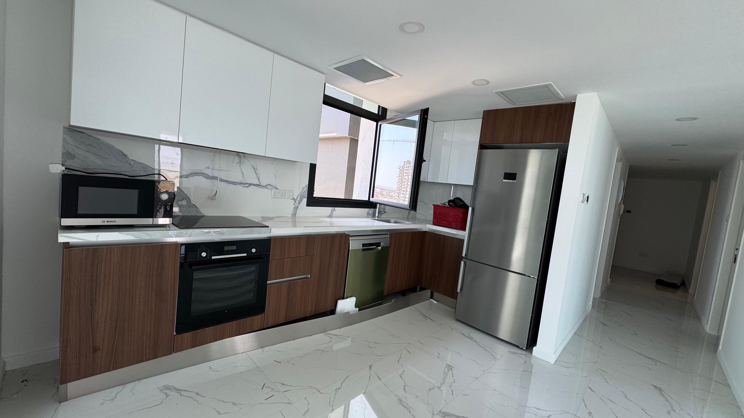 kıbrıs Beyaz ve ahşap dolaplar, paslanmaz çelik aletler, mermer desenli zemin ve backsplash, tezgah üzerinde bir mikrodalga fırın ve lavabonun üzerinde bir pencere bulunan modern mutfak, İskele Long Beach satılık daire aramanız için mükemmeldir. Sağ tarafta bir koridor uzanmaktadır. aysan_giti