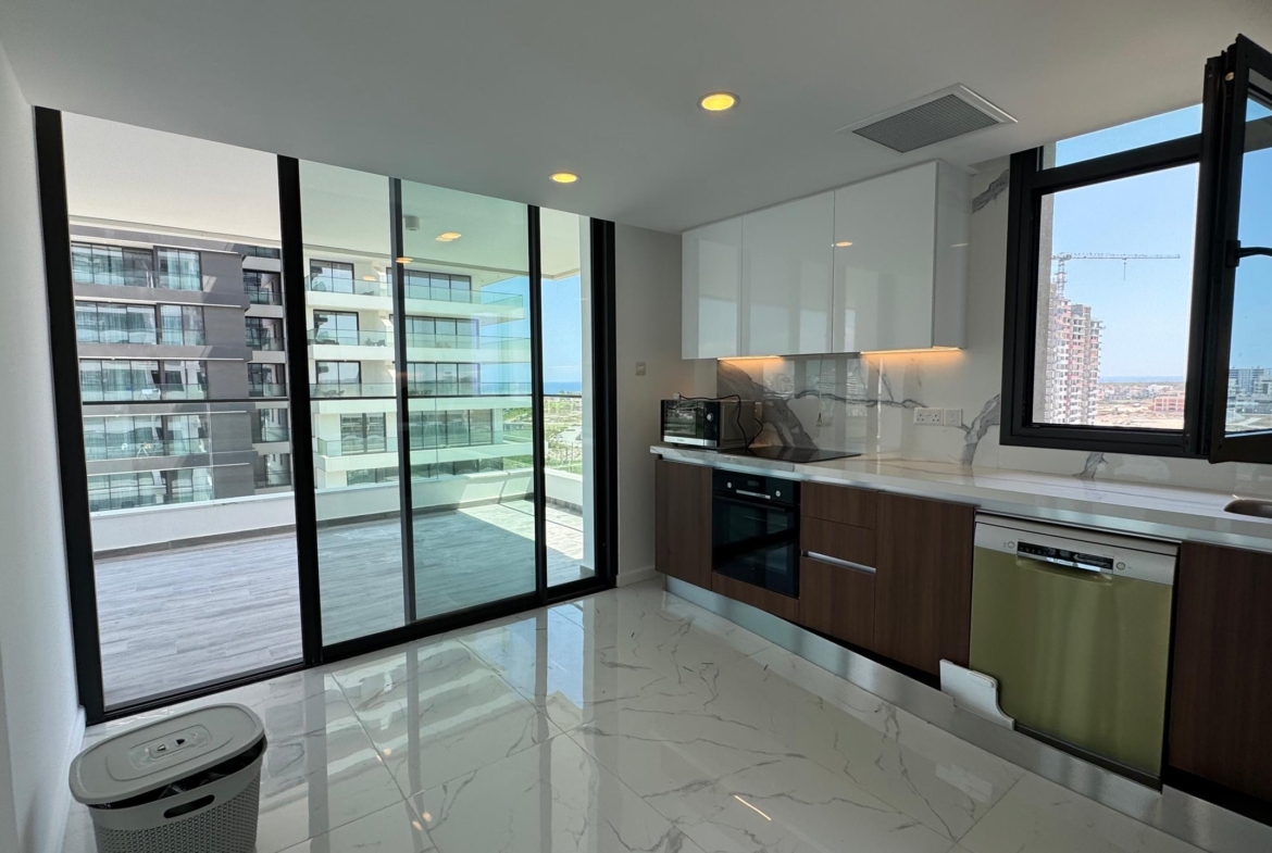 kıbrıs Beyaz ve ahşap dolaplar, ankastre cihazlar ve büyük pencereli modern mutfak. Cam kapılar, şık bir Kuzey Kıbrıs satılık daire arayanlar için ideal olan şehir manzaralı geniş bir balkona açılmaktadır. Mermer desenli zeminler aydınlık ve havadar mekânı zenginleştirmektedir. aysan_giti
