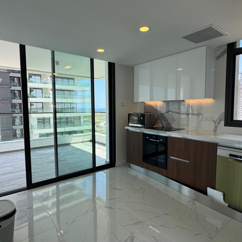 kıbrıs Beyaz ve ahşap dolaplar, ankastre cihazlar ve büyük pencereli modern mutfak. Cam kapılar, şık bir Kuzey Kıbrıs satılık daire arayanlar için ideal olan şehir manzaralı geniş bir balkona açılmaktadır. Mermer desenli zeminler aydınlık ve havadar mekânı zenginleştirmektedir. aysan_giti