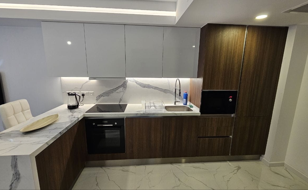kıbrıs Beyaz mermer tezgah ve backsplash, ahşap dolaplar, ankastre fırın, paslanmaz çelik evye, kahve makinesi ve bulaşıklık içeren modern mutfak. Temiz çizgiler ve nötr renklerle minimalist tasarım. aysan_giti