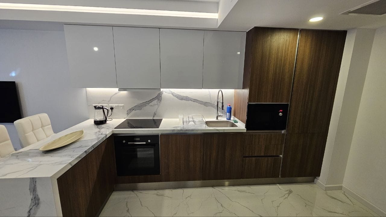 kıbrıs Beyaz mermer tezgah ve backsplash, ahşap dolaplar, ankastre fırın, paslanmaz çelik evye, kahve makinesi ve bulaşıklık içeren modern mutfak. Temiz çizgiler ve nötr renklerle minimalist tasarım. aysan_giti